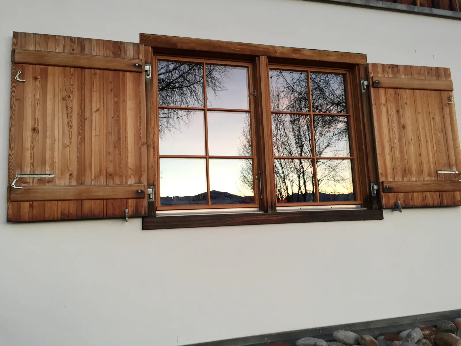 Lärchen-Fensterläden der Casa Seglias, im Fenster spiegelt sich der Abendhimmel