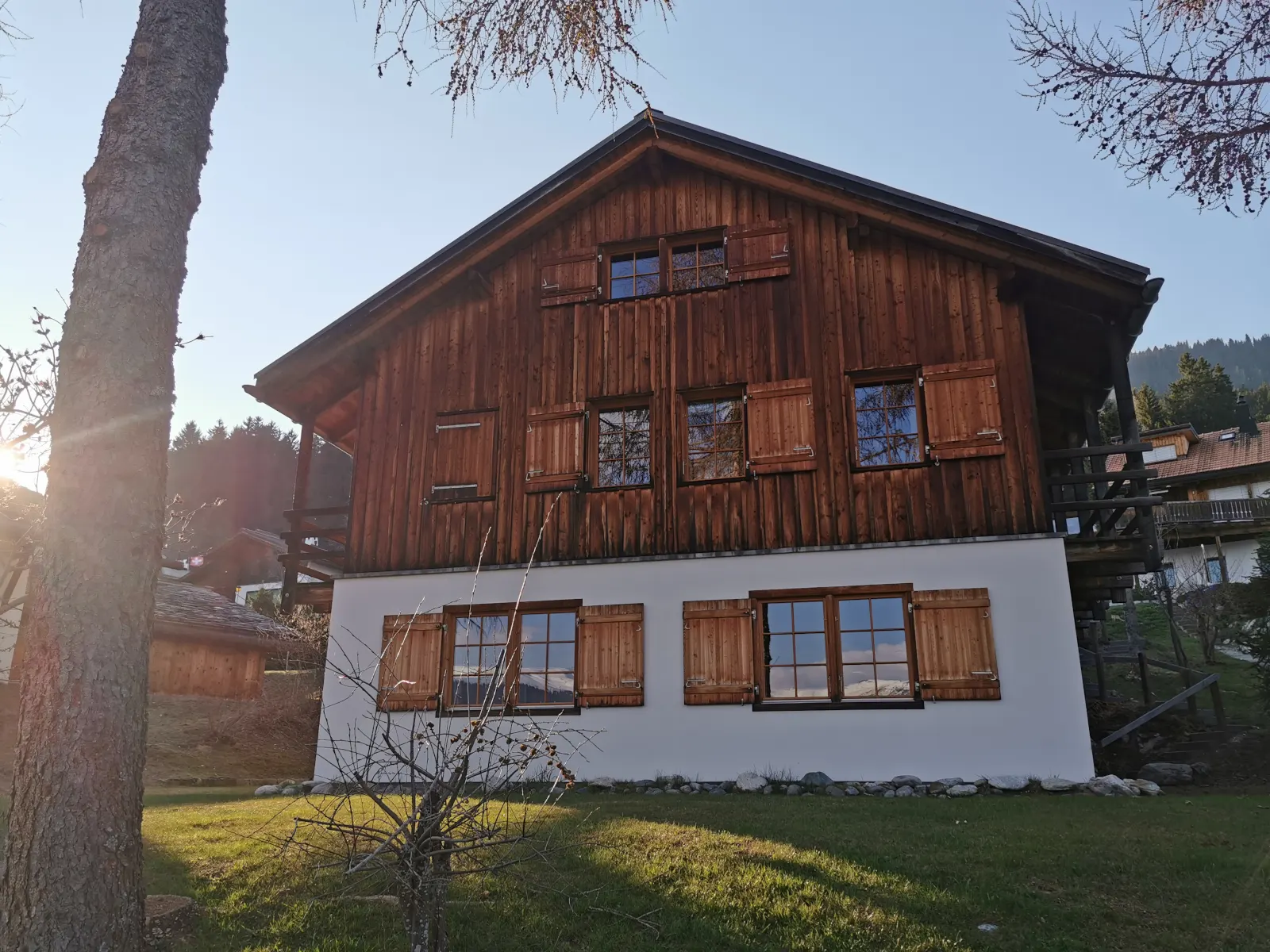 Casa Seglias vom Garten aus: Holzfassade mit Lärchen-Fensterläden in der Abendsonne