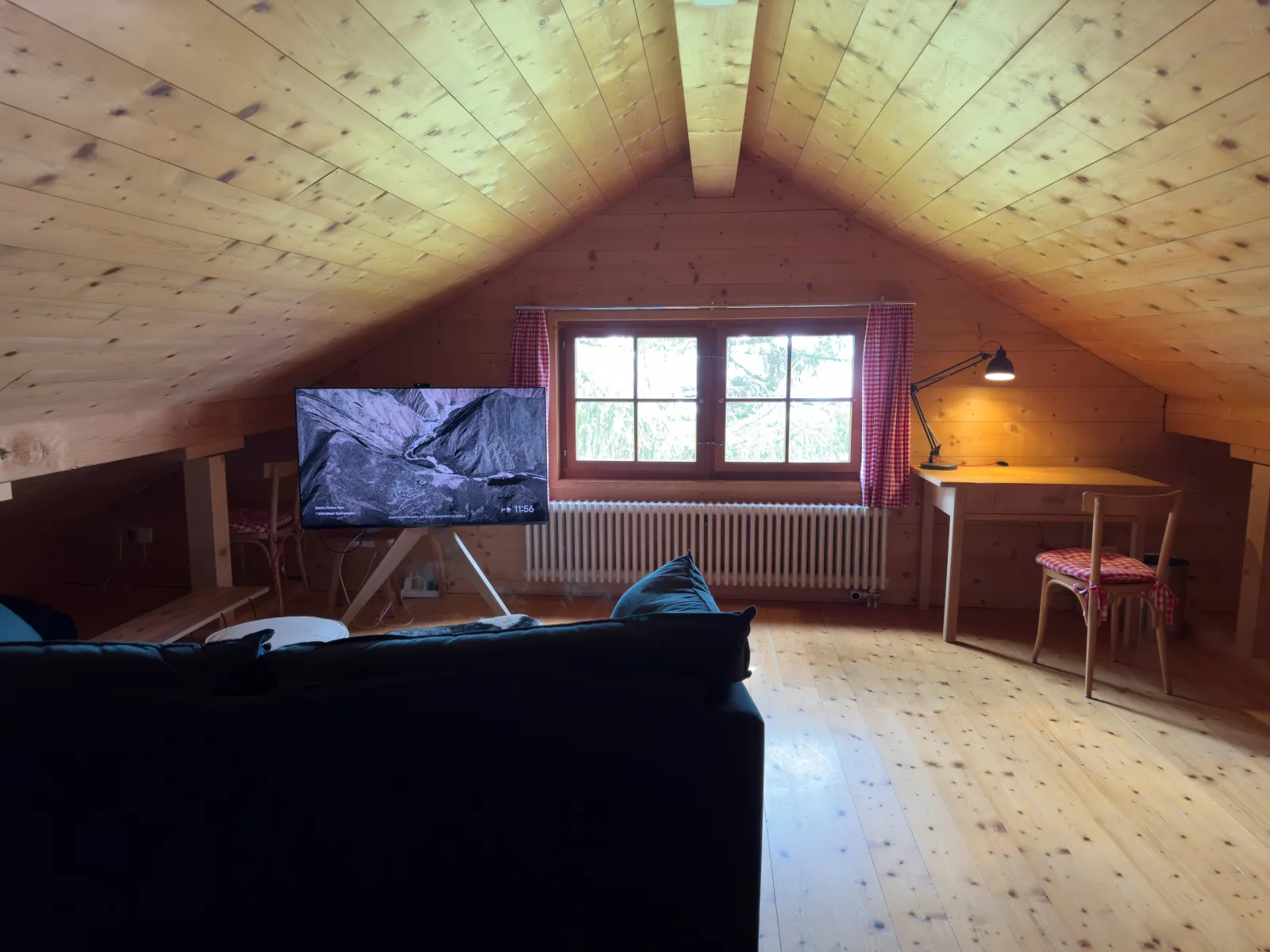 Dachgeschoss mit Sofa, 55-Zoll-Fernseher und Schreibtisch unter der Giebeldecke aus hellem Holz