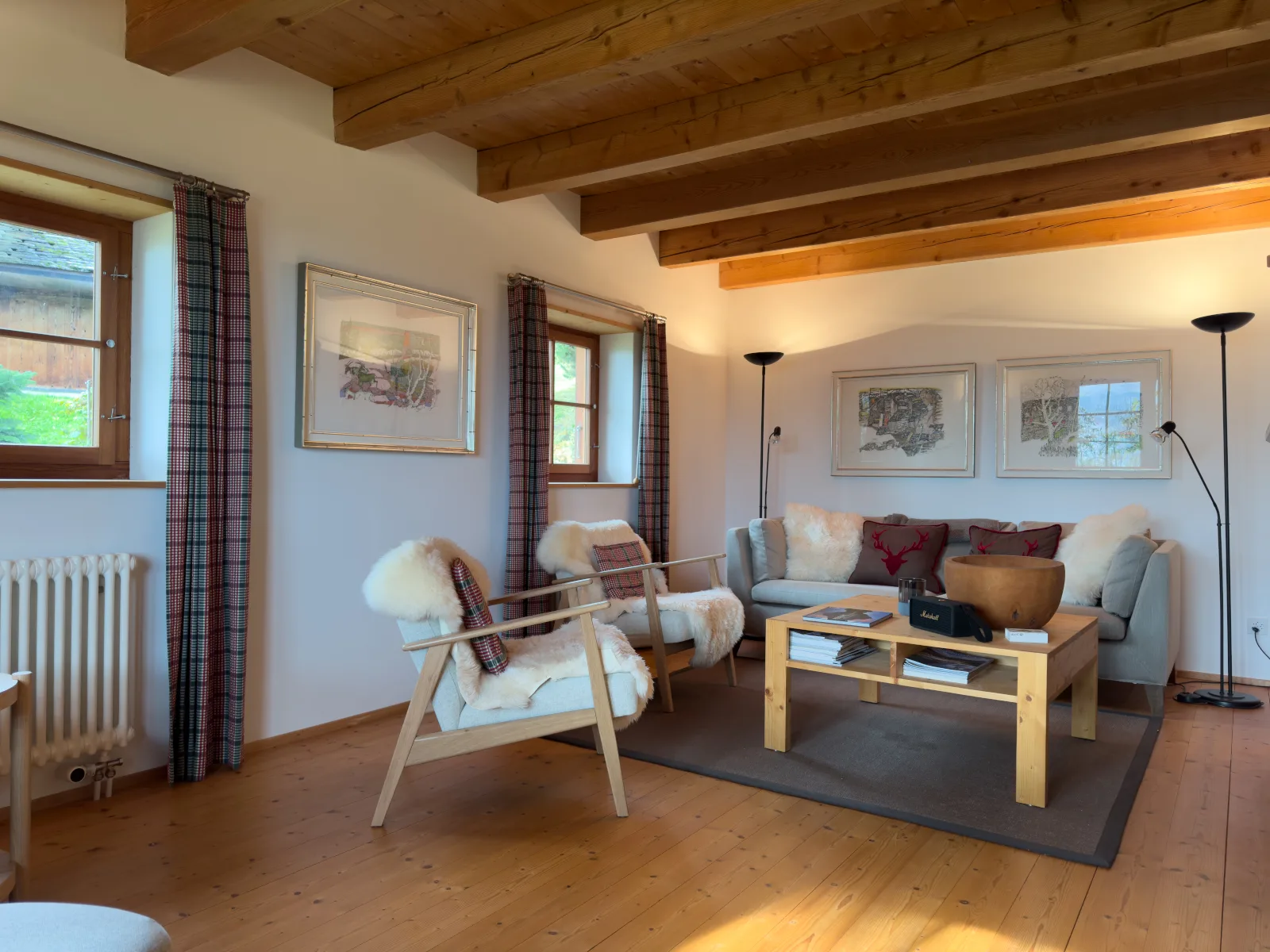 Wohnzimmer der Casa Seglias: Balkendecke, helle Sessel mit Schaffellen und Sofa unter Originalgemälden