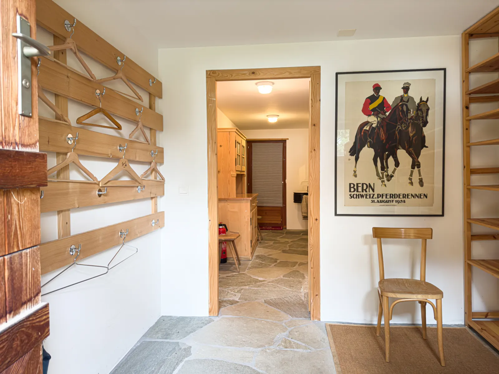 Eingangsbereich mit Steinboden, Garderobe und einem alten Plakat der Berner Pferderennen von 1924