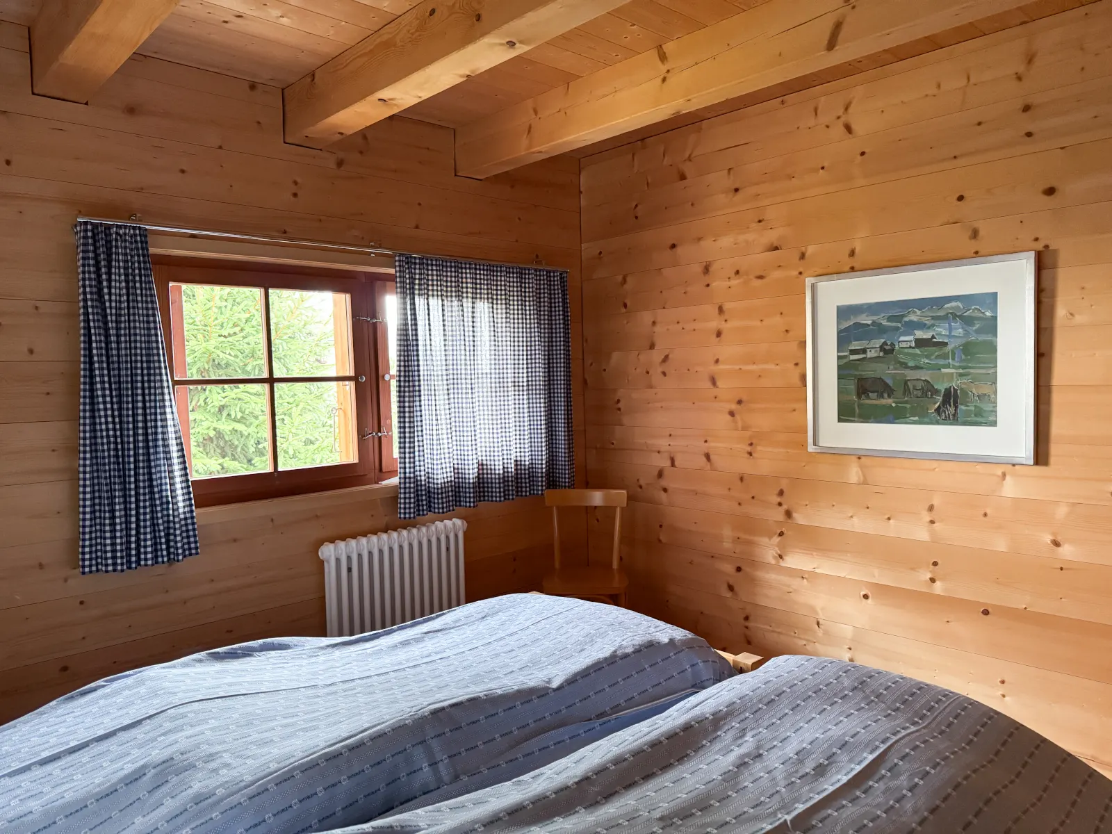 Doppelzimmer mit blau karierten Vorhängen und einem Gemälde einer Alpweide
