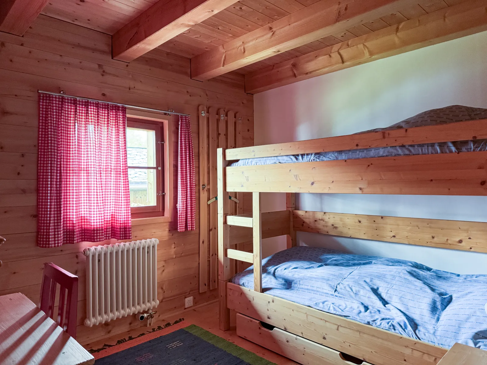 Kinderzimmer mit Kajütenbett, rot karierten Vorhängen und kleinem Schreibtisch mit rotem Stuhl